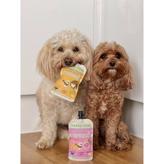 Two dogs with a bottle of Hearty Licks pet product on a wooden floor.