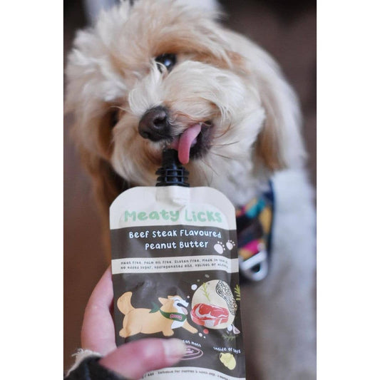 Dog licking a 'Meaty Licks' pet treat container with a visible brand logo.