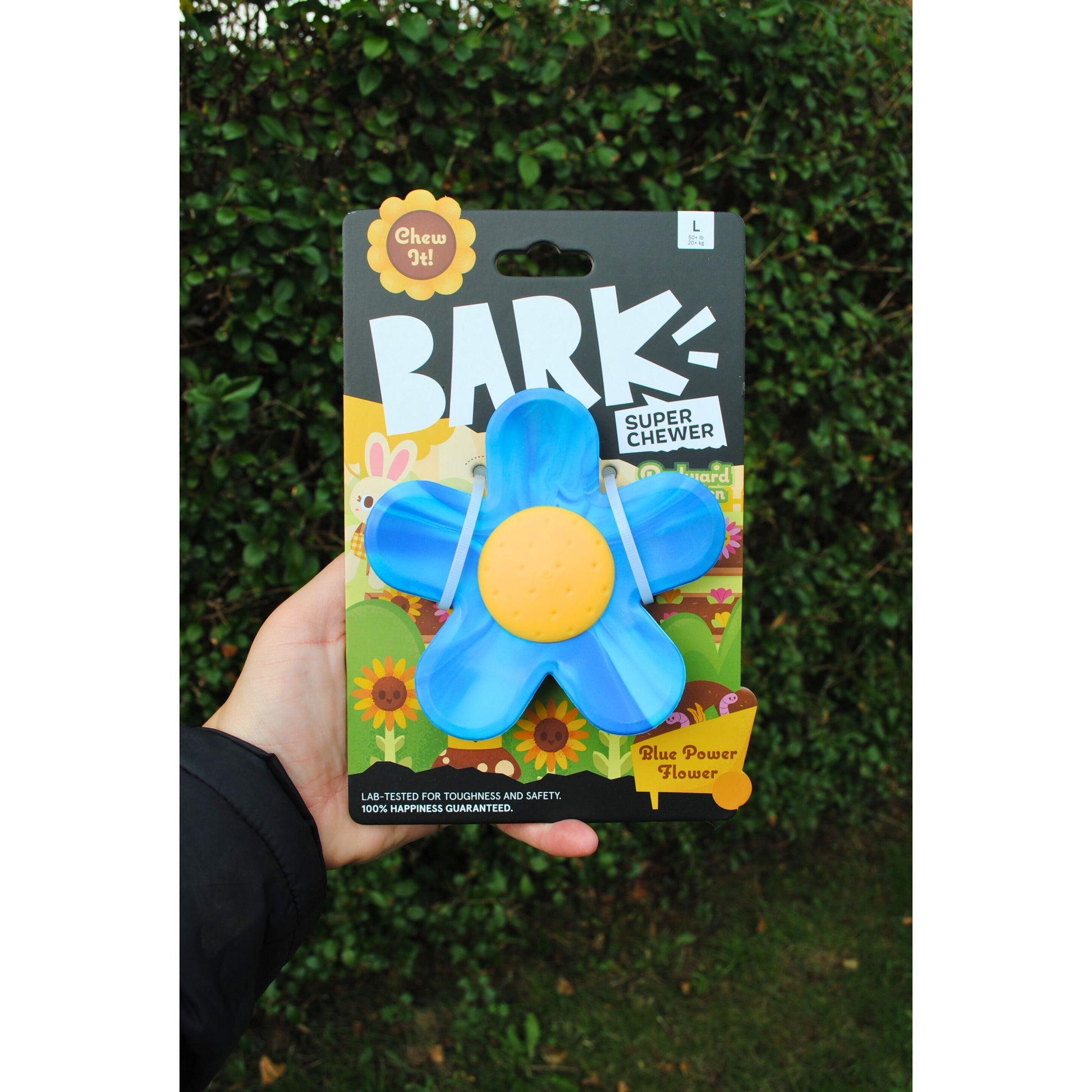 Hand holding a package of a blue flower-shaped dog chew toy with 'BARK!' branding.