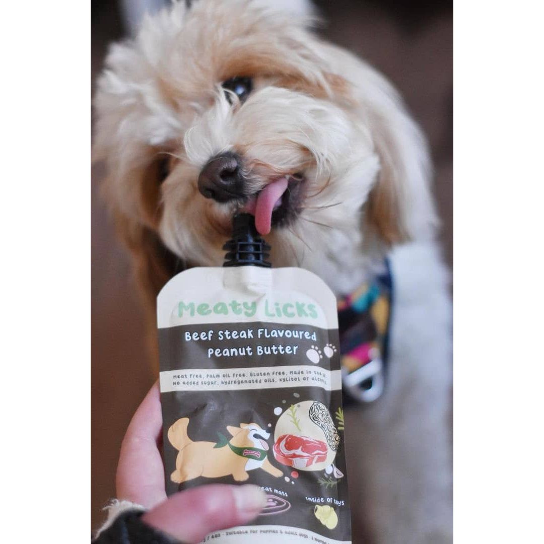 Dog licking a 'Meaty Licks' pet treat container with a visible brand logo.